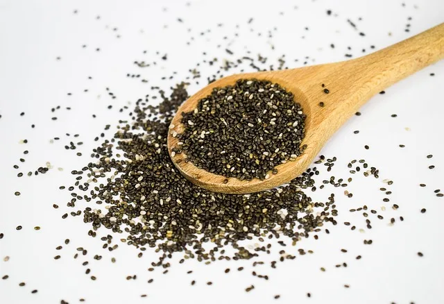 Colher de madeira cheia de sementes de chia sobre uma mesa rústica, destacando a textura do superalimento.